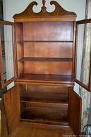 Interior view of the cabinet with glass doors open showing three upper shelves and two-door lower storage with one shelf inside.