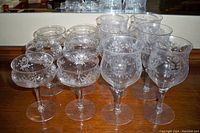 Set of 12 vintage etched crystal goblets featured in two rows, showing the variation in height and detailed floral etching on clear glass.