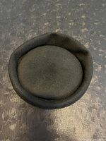 Top down view of the black felt pill box hat showing its rounded closed crown and rolled brim edge.