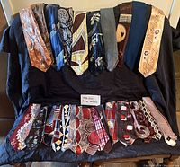 Full display of more than 20 vintage neckties laid out on a black cloth background, showing various patterns and colors typical of 1940s-1950s design.
