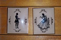 Two framed silhouette pictures displaying an English man and woman in traditional dress. Both pieces have floral decorative borders and appear lightly used.