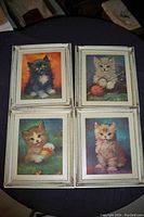 Four framed pictures of kittens from the 1960s in plastic frames, arranged in a 2x2 grid, photographed on a dark surface with surrounding items partially visible.