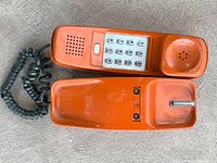 Top and side view of bright orange Princess phone handset with push-button dial keypad and coiled cord.
