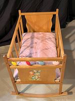 Front view of wooden rocking cradle showing painted bunny decoration on foot panel and pink mattress inside.