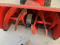 Close-up of the red snow blower auger showing wear, surface rust, and design details of the blade assembly.