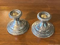 Front and angled top view of two silver candleholders showing detailed rims and tarnish.
