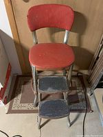 Front view of red vintage step stool showing red seat and backrest with two black wooden steps and metal frame.