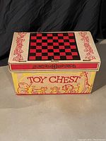 Rectangular cardboard vintage toy chest box with colorful graphic illustrations and checkerboard pattern on lid.