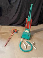 Toy vacuum cleaner with various plastic attachments laid out on floor in front of black fabric backdrop.