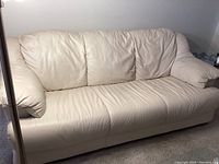 Full front view of bone-colored leather sofa showing three seat cushions and padded arms