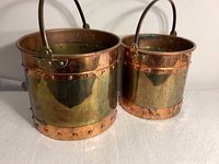 Front and side view of two of the copper and brass buckets showing rivet details and metal handles.