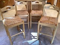 Four wooden barstools with thatched seats arranged together in kitchen area, showing overall condition and style