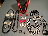 Overview of all jewelry items arranged on table showing necklaces, earrings, bangles and pin in black, white, and red