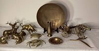 Full view of brass animals including deer, bull, squirrel, crab; large brass bowl; miniature cannon; brass ashtray and bowl on table.