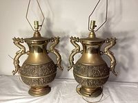 Pair of solid brass dragon-handled lamps showing full front view on white surface