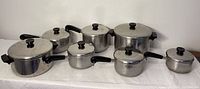 Overall set of stainless steel Revere Ware pots with black handles and lids with knobs.
