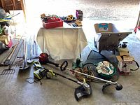 Overview of two string trimmers, lawn cart, irrigation supplies, extension cord, and small tools on floor