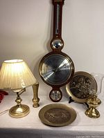 Full view of the barometer, lamps, plates, and vase arranged on a white table surface with a white wall backdrop.