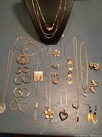 Full view of lot including necklaces on stand, multiple earrings, a ring, and a flower pin all in gold tone.