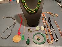 Full lot view of natural stone jewelry including necklaces, pendants, earrings, bracelets, and a ring on a flat surface with display bust