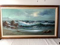 Full view of the framed seascape painting depicting waves crashing on rocky shore under a moody sky.