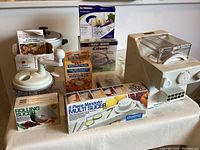 Wide shot of Pasta Express electric pasta maker with boxes of kitchen gadgets including onion chopper, mandolin slicer, rolling slicer, and onion blossom maker kits.