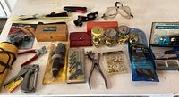 Overview of various random hardware and hand tools including punch sets, wire cutters, staple gun, safety glasses, zip ties and jars of grommets.
