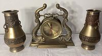 Front view showing the clock flanked by two matching vases, all solid brass with dragon decorations.