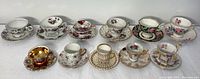 Wide view of all 11 vintage porcelain teacups and saucers in varied floral and gold designs.