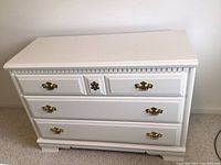 Front view of white Bassett 3-drawer dresser showing brass handles and decorative molding.