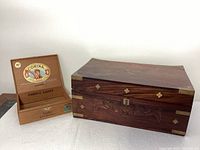 Closed rectangular carved wooden box with brass protective corners and decorative brass studs on surface edges. Key inserted in lock on front panel.