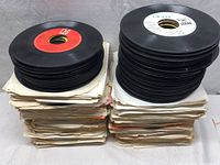 Stacks of approximately 45 RPM vinyl records on paper sleeves in two columns, showing quantity and condition of sleeves and records.