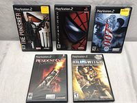 Photo of five PlayStation 2 game cases including The Punisher, Spider-Man, 007: Everything or Nothing, Resident Evil Outbreak, and Kill Switch, arranged in two rows on grey fabric.