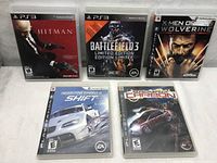 Five PS3 games displayed: Hitman Absolution, Battlefield 3 Limited Edition, X-Men Origins Wolverine, Need for Speed Shift, and Need for Speed Carbon.