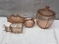 Lot of four pink Depression glass collectible items displayed on white cloth background