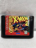 Front view of Sega Genesis X-Men 2 Clone Wars game cartridge showing label artwork with signs of wear and damage.