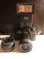 Vivitar V335 camera with attached zoom lens, two additional lenses and Vivitar flash on top.