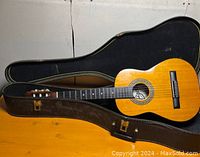 Acoustic guitar placed inside an open black hard case on a wood surface.