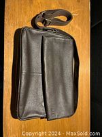 Black pebbled leather satchel with front flap and shoulder strap on wooden surface.