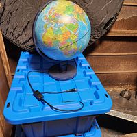 Light up globe on black plastic base with semi-meridian holder placed on a blue plastic bin. Power cord with inline switch is visible.