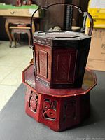 Photo showing the red wood octagon plant stand topped with the bamboo wedding basket, highlighting the carved wood panels and the basket handle.