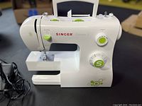 Front and left view of white Singer Esteem II model 2273 sewing machine showing controls and green accent dials.