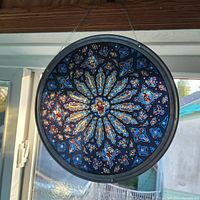 Front view of round stained glass art highlighting vibrant colors and intricate design hung by string.