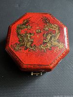 Top view of octagonal red lacquered wooden jewelry box with gold dragon motifs and front metal latch closure