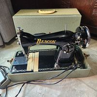 Front and side view of black Beacon sewing machine inside green carrying case with lid open.