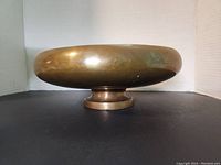 Side view of the brass pot showing rounded bowl mounted on short pedestal base with patina and tarnish marks.