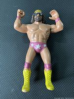 Front view of Macho Man Randy Savage wrestling figure with arms raised wearing purple trunks with stars and yellow boots.