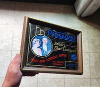 Photo showing the front of the vintage Pepsodent advertising mirror with visible text and illustration, held in hand for scale.