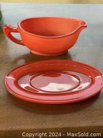 Front view of the red gravy boat and matching saucer on table showing shape and color.