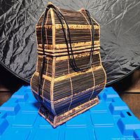 Front right angled view of the woven wicker basket bag showing curved shape and black cords